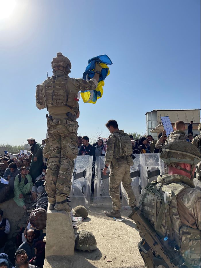 En soldat står uppe på en mur och viftar med en svensk flagga. Foto.