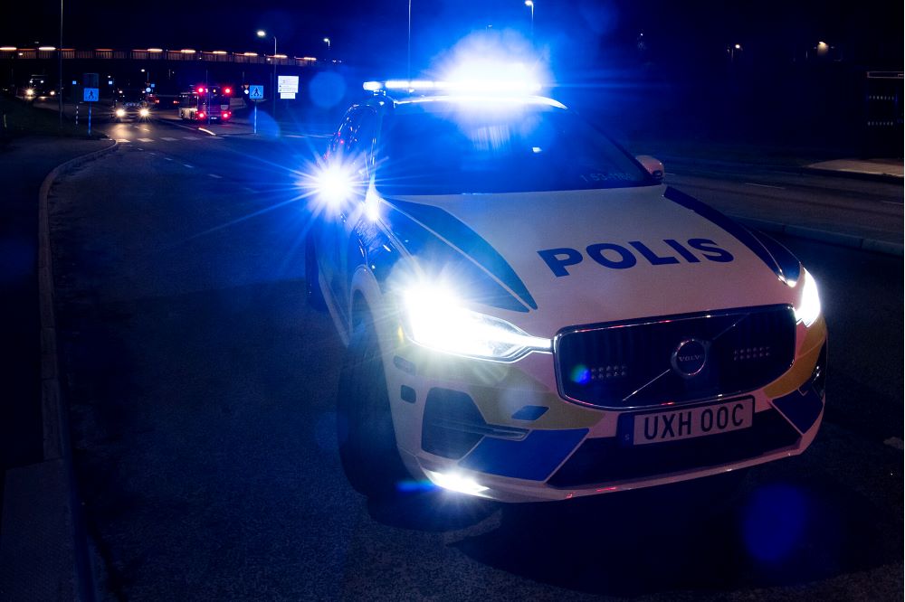 En polisbil står på en mörk gatan med blåljus tända