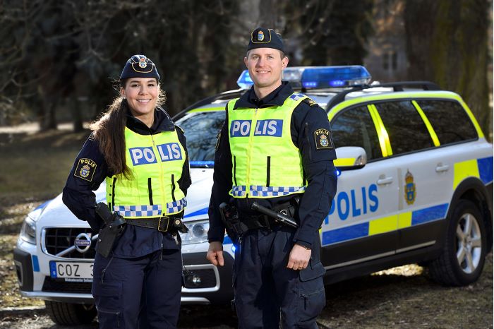 Två uniformerade poliser med en polisbil i bakgrunden.