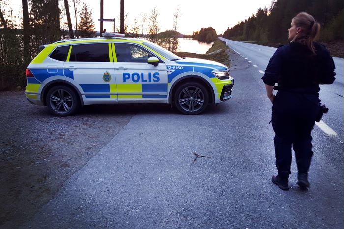 Polis står vid sidan av vägen bredvid polisbil.