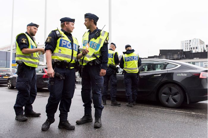 Poliser i samspråk. Två poliser i bakgrunden som genomför en fordonskontroll.