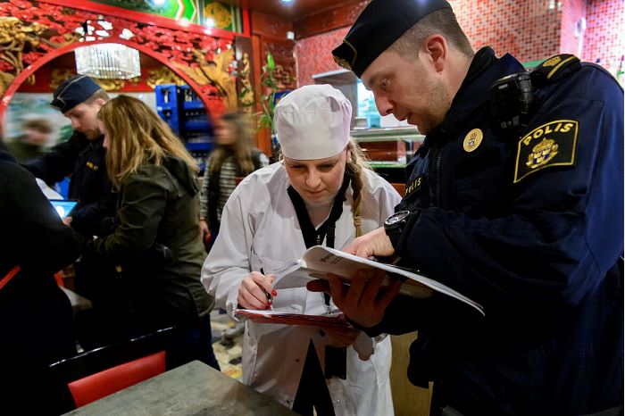 Person står med en polis i ett resturangkök.