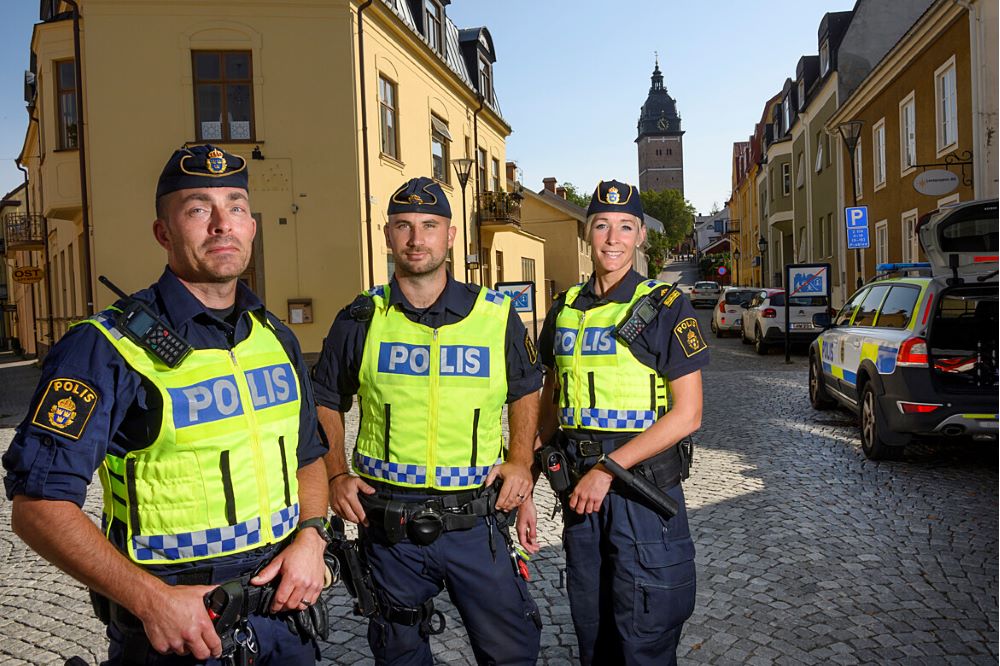 Två män och en kvinna klädda i polisuniform och varselväst tittar rakt in kameran.