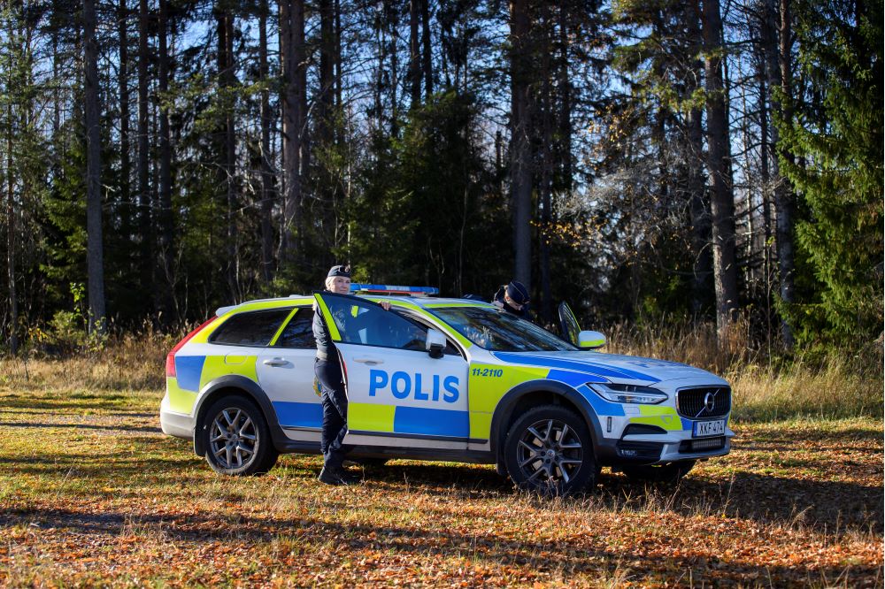 Poliser står vid en polisbil. Det är höst.