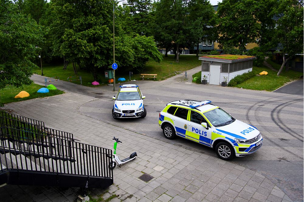 Två bilar på en gata i ett bostadsområde med flerfamiljshus, bilden är tagen uppifrån