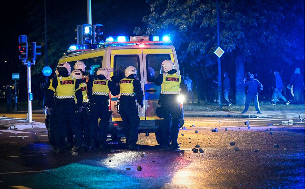 Natt. Poliser framför polisbuss, stående med ryggen mot kameran.