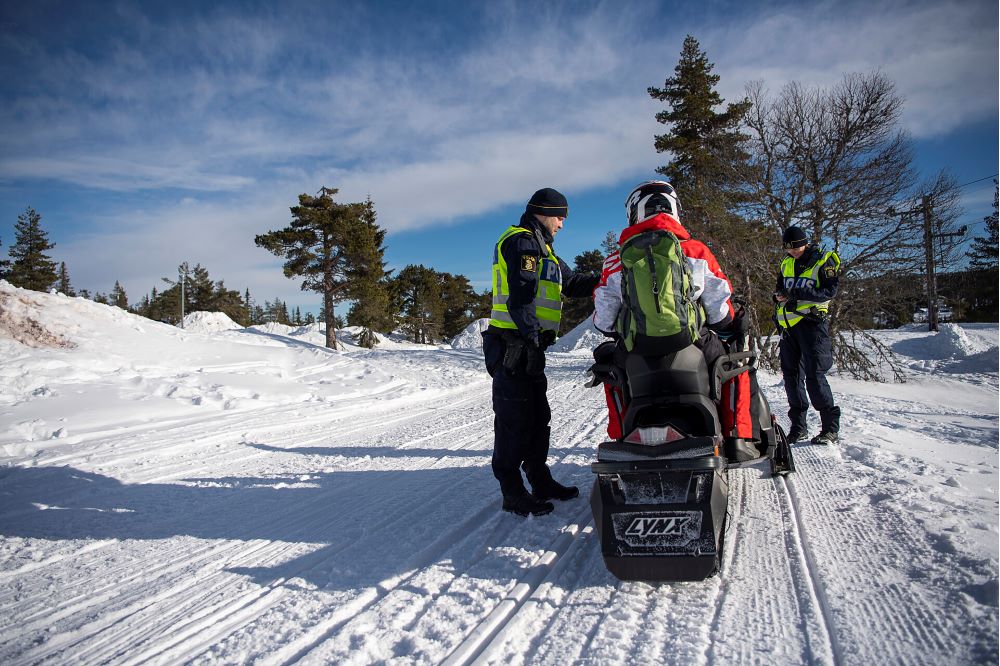 Polisen håller en kontroll på vintern. Snö på marken. Polisen kontrollerar en snöskoterförare.