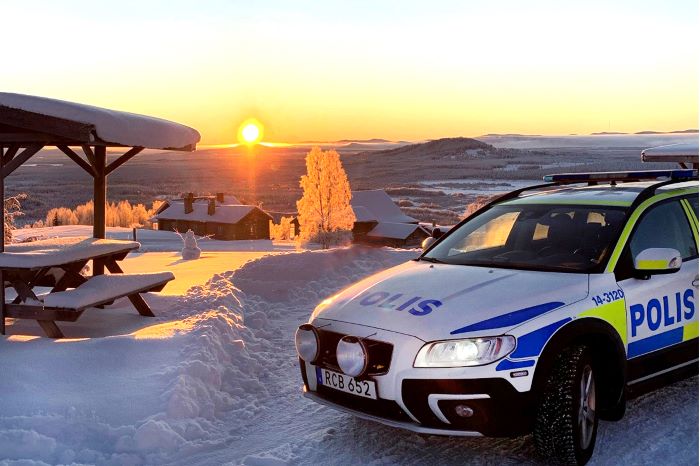 Polisbil som står på snöigt berg med solnedgång.