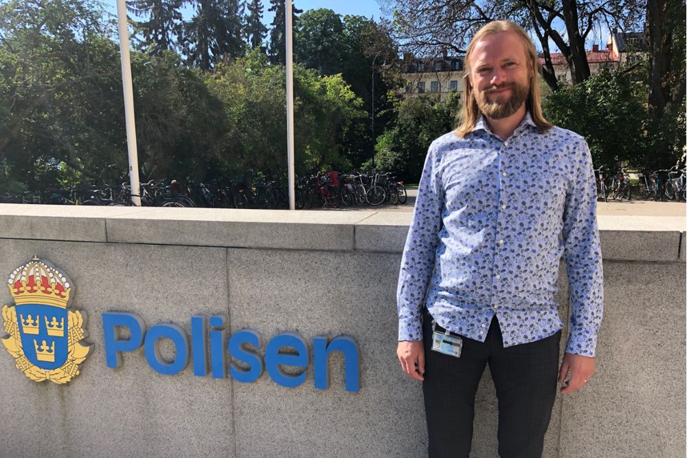 Jonas står vid entrén till polishus och har polisloggan bredvid sig.