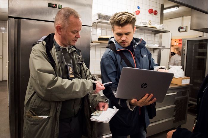 Person står med en polis i ett resturangkök under en kontroll.