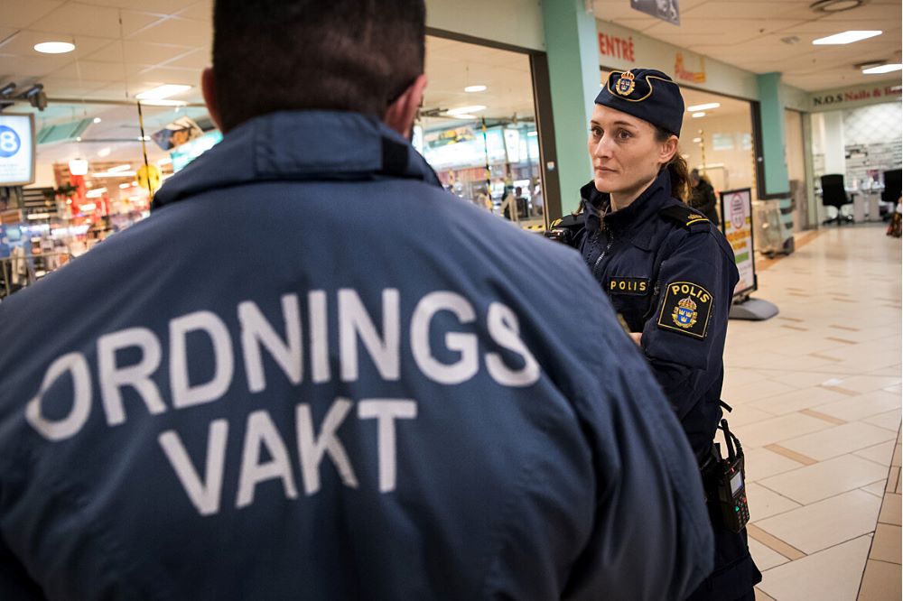 Ryggen på en ordningsvakt som står och pratar med kvinnlig polis