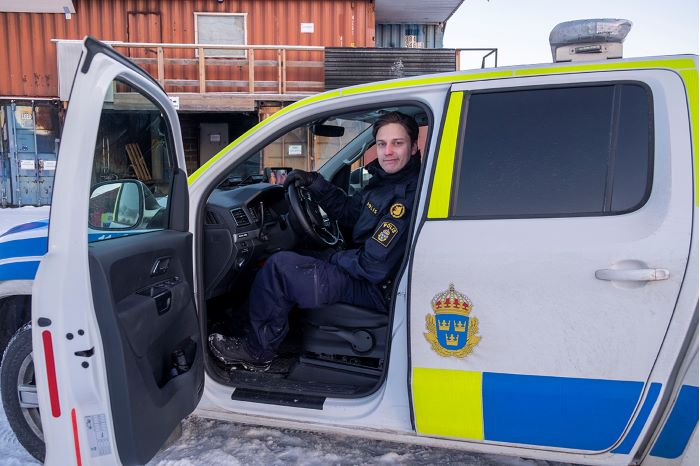 Polisklädd person sitter i polisbil med förardörren öppen