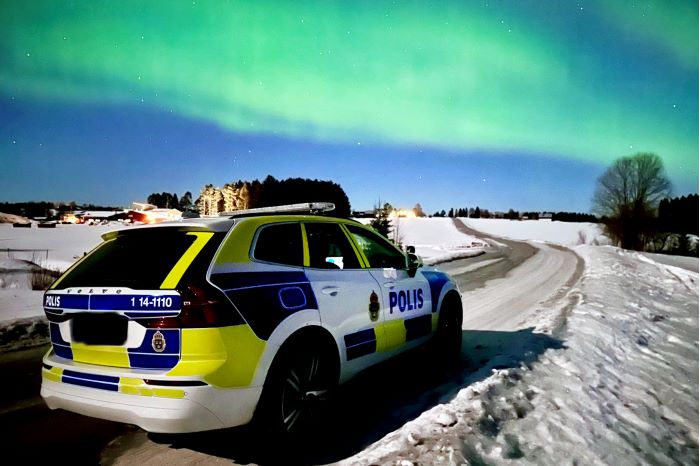 Polisbil som står på snöig väg med norrsken.