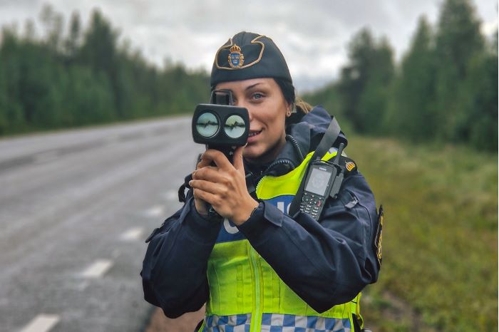 Polis står med hastighetsmätare vid väg.