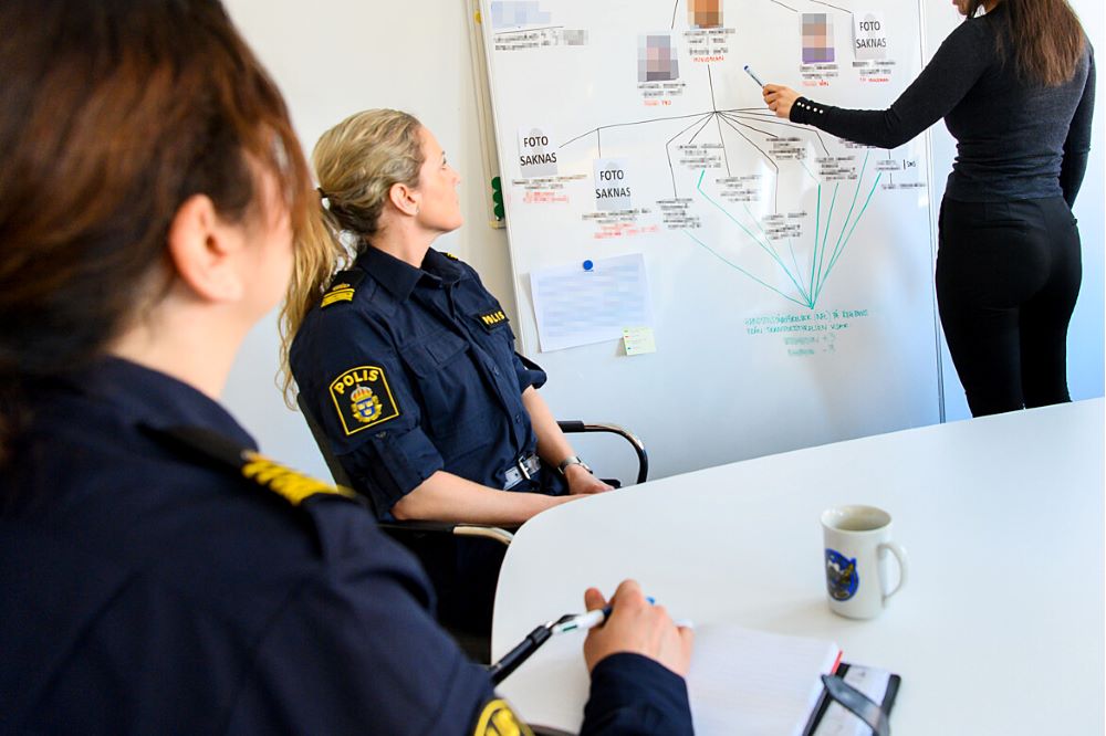 två uniformerade poliser vid ett bord och en civilanställd vid whiteboard