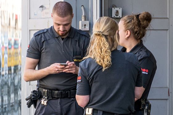 Tre väktare står i grupp och samtalar. En av dem tittar i en mobiltelefon.