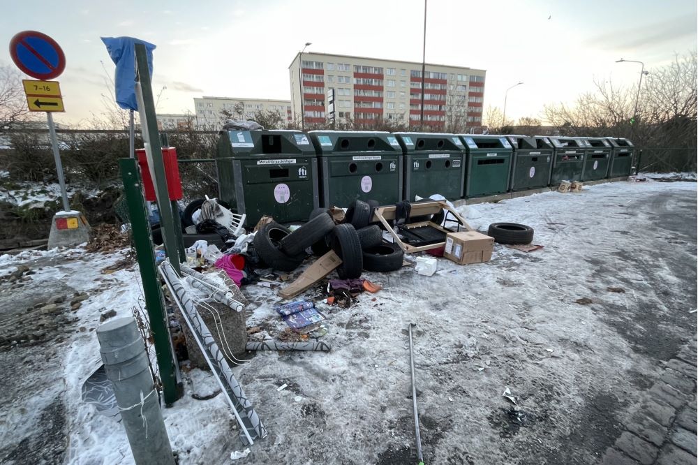 Sopor utanför behållare, bland annat bildäck. Höghus i bakgrunden.